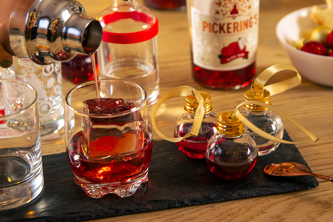 Person pouring a drink into a glass with small bottles of liquor on a wooden table.